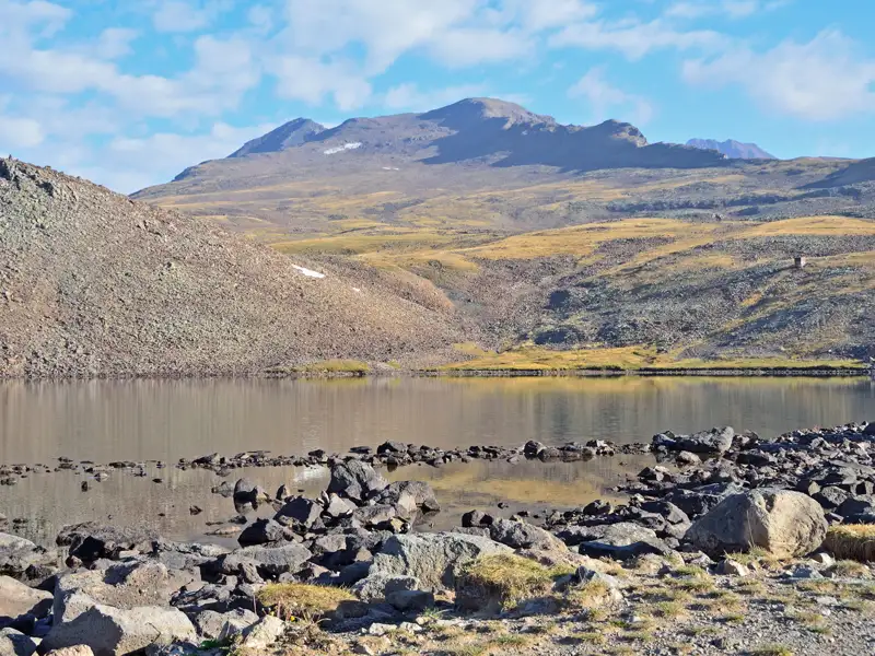 Bergsee mit felsigem Ufer und Blick auf das Bergmassiv.