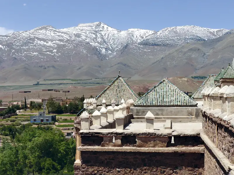 Traditionelle Architektur mit grün glasierten Ziegeln vor schneebedeckten Bergen.
