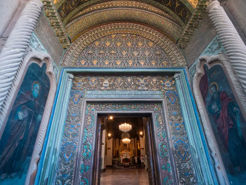 Verziertes Kirchenportal mit Heiligenbildern und Blick in das Kircheninnere.