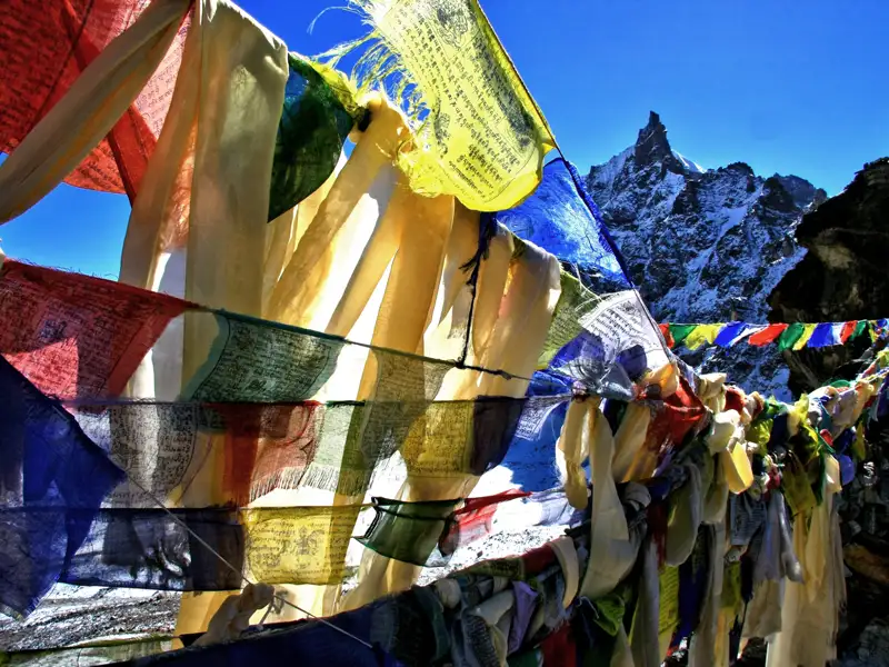 Gebetsfahnen im Wind mit Berggipfel im Hintergrund.
