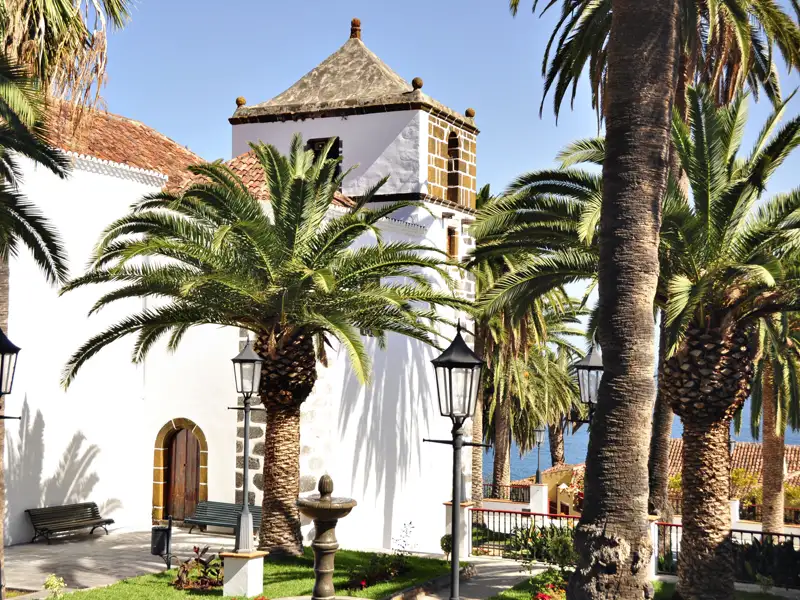 Weiße Kirche mit Glockenturm und Palmen.