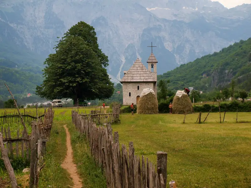 Kleine Kirche in ländlicher Umgebung mit Bergen im Hintergrund.