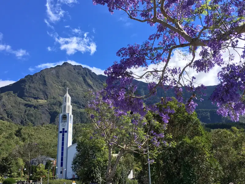 Weiße Kirche mit Bergkulisse und blühendem Baum.
