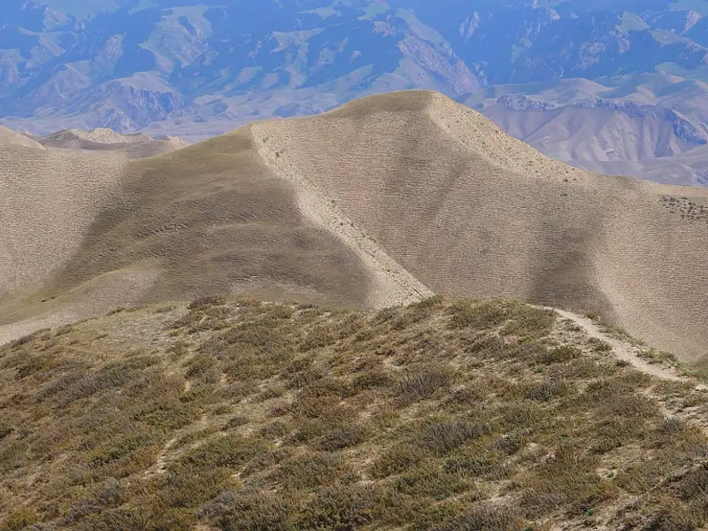 Sandige Hügel und ein schmaler Pfad in einer Berglandschaft.