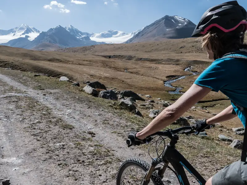 Mountainbiker auf einem Bergpfad mit schneebedeckten Gipfeln im Hintergrund.