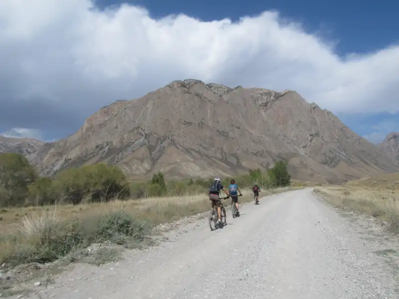Drei Mountainbiker auf einer Schotterstraße in bergigem Gelände.