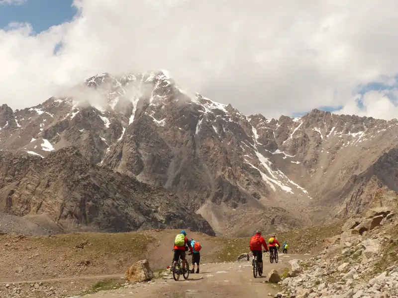 Mountainbiker auf einer Bergstrecke mit schneebedecktem Gipfel im Hintergrund.