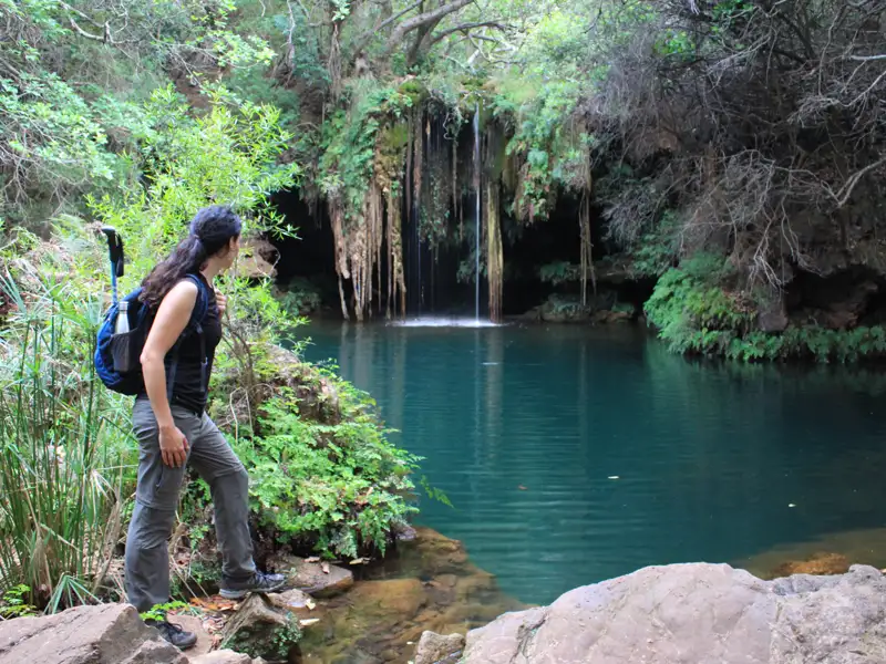 Wanderer am Ufer eines türkisfarbenen Teichs mit Wasserfall.