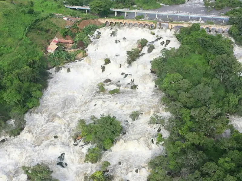 Luftansicht der Stromschnellen eines Flusses mit einer Brücke im Hintergrund.