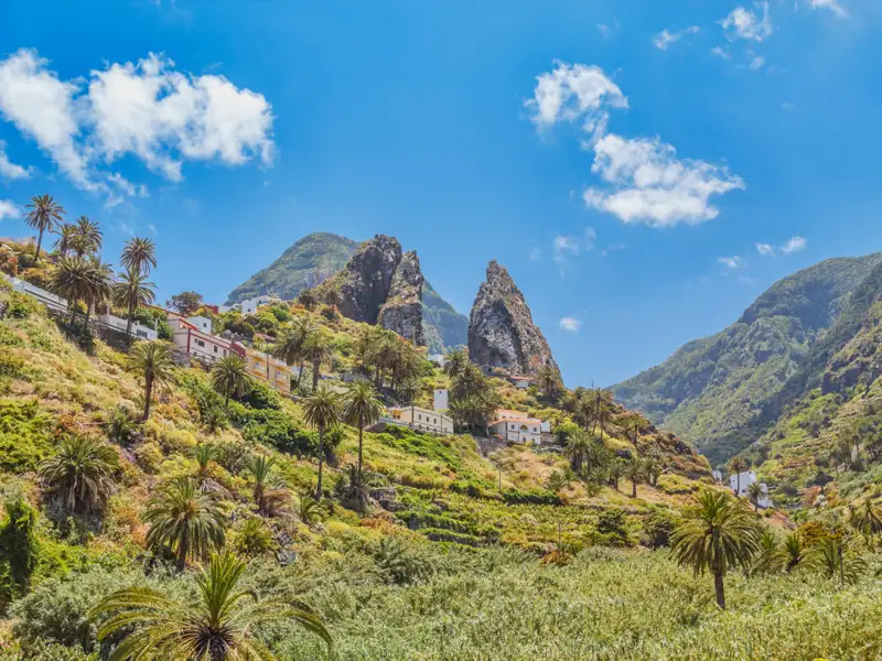 Ein Dorf inmitten einer hügeligen Landschaft mit Palmen und einzigartigen Felsformationen.