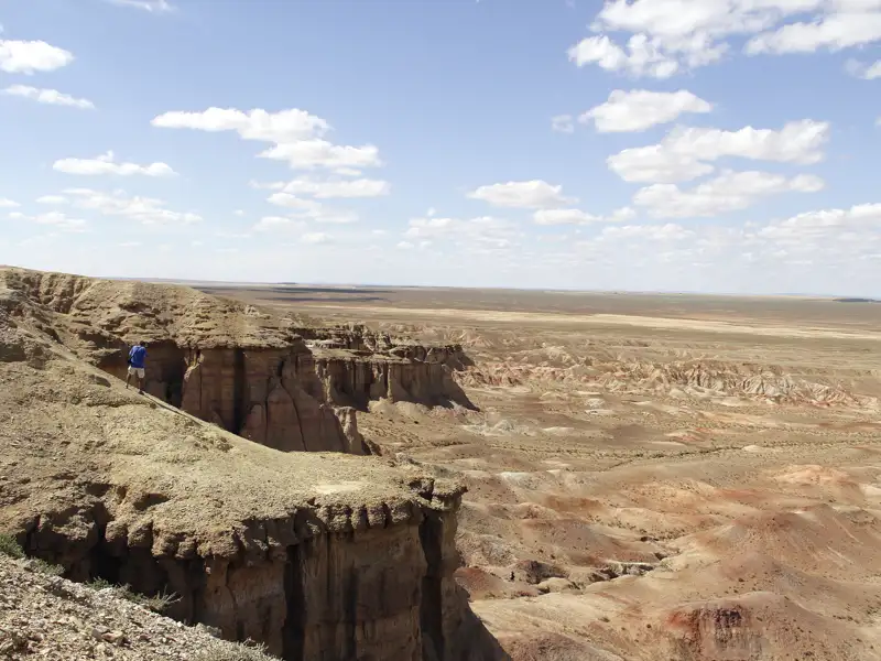 Reisender am Rand einer Klippe mit Blick auf eine weitläufige Wüstenlandschaft.