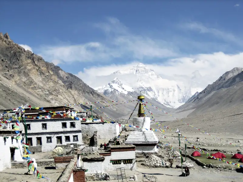 Blick auf den Mount Everest von einem tibetischen Kloster aus. Gebetsfahnen und eine Stupa sind im Vordergrund sichtbar.