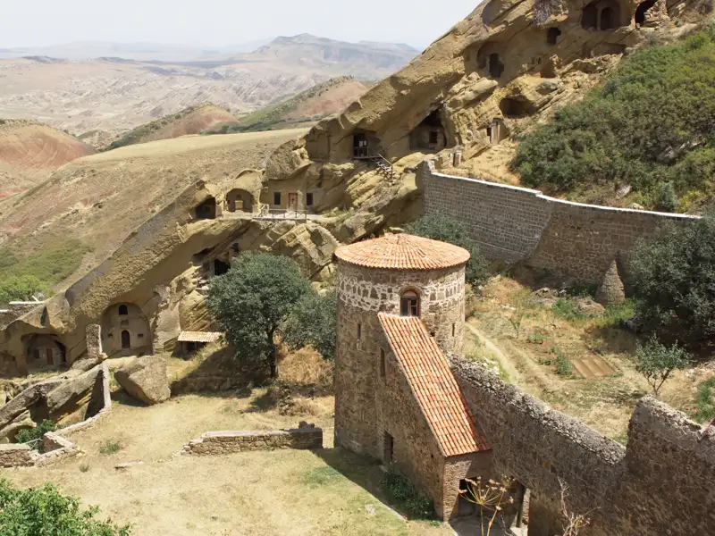 Schneebedeckte Berggipfel im Hintergrund, grüne Hügel und Bäume im Vordergrund.
