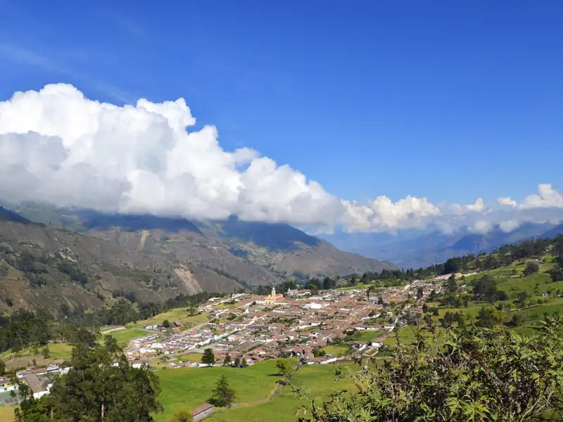 Blick auf ein Andendorf mit umliegenden Bergen und Wolken.