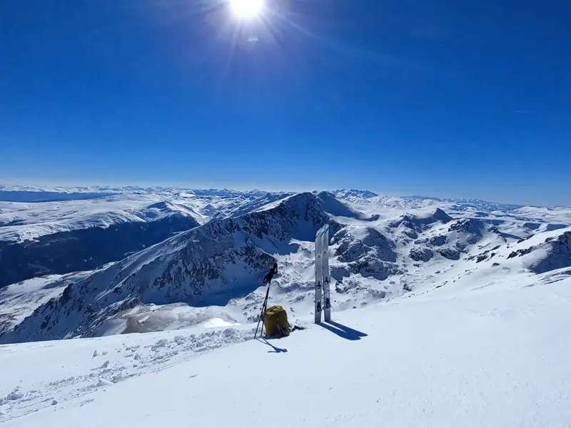 Skiausrüstung auf einem sonnigen Berggipfel mit Panoramablick auf die verschneite Bergkette.