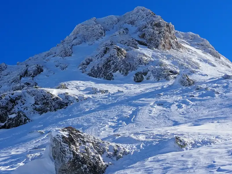 Verschneiter Berghang mit sichtbaren Spuren im Schnee, möglicherweise von Skifahrern oder Snowboardern.