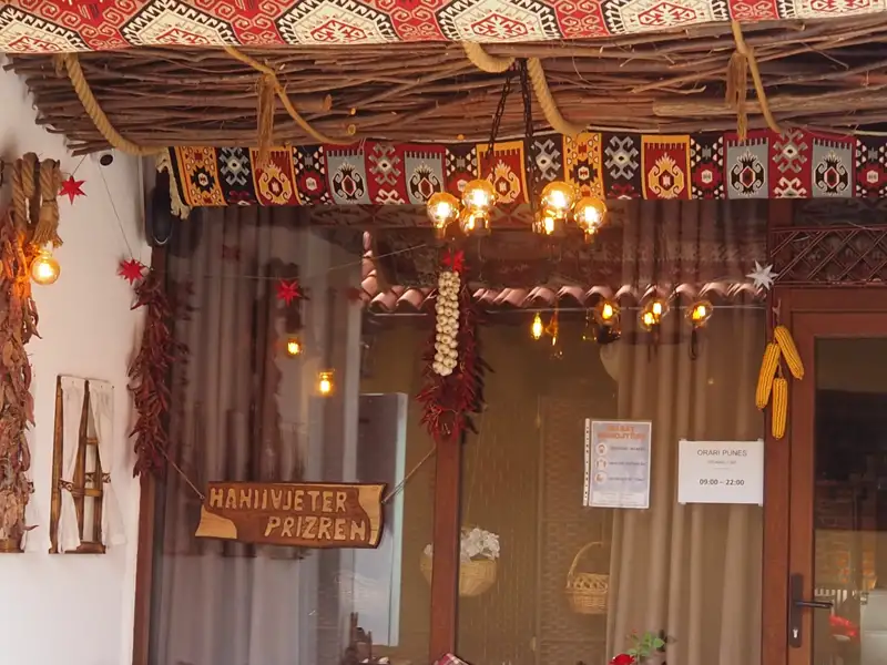 Traditionell dekorierter Eingang des Hanivjeter Restaurants in Prizren mit Teppichen, Beleuchtung und lokalen Elementen.