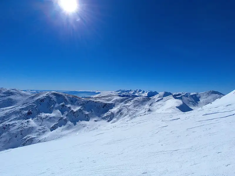 Panoramablick auf eine verschneite Bergkette unter einem klaren blauen Himmel.
