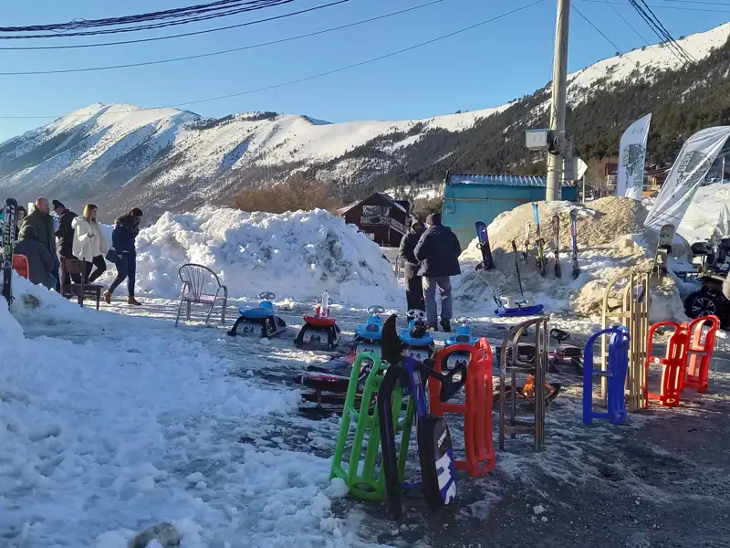 Schlitten, Schneesportgeräte und Menschen in einer verschneiten Berglandschaft.