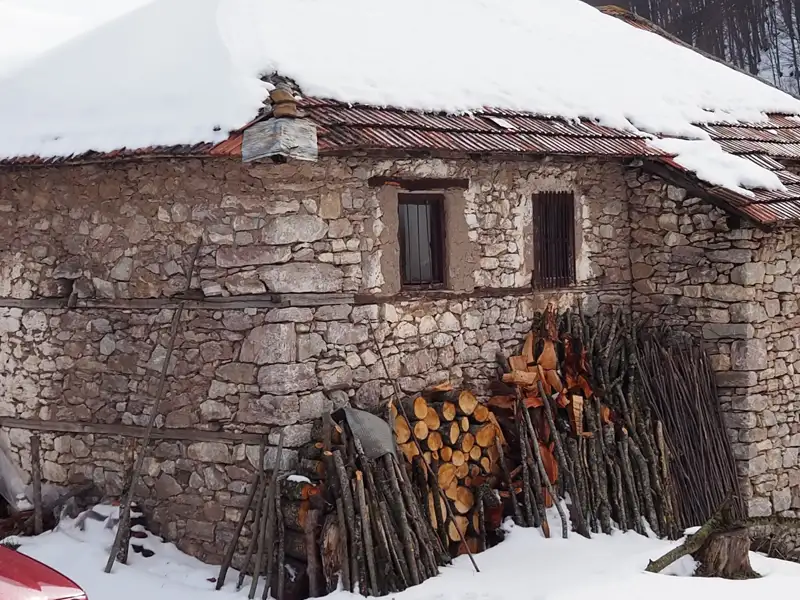 Verschneites Steinhaus mit Brennholzvorrat.