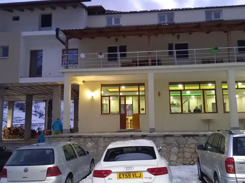 Das Hotelgebäude bei Dämmerung mit parkenden Autos und leichtem Schneefall.