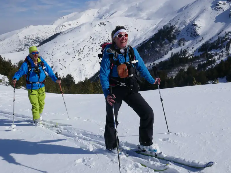 Zwei Skitourengeher mit Stöcken und Skiern in einer verschneiten Berglandschaft.