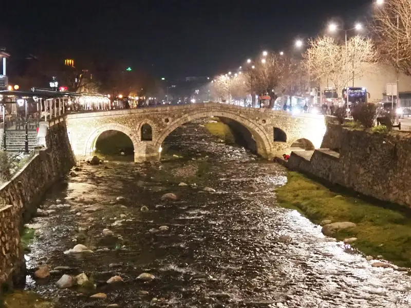 Beleuchtete Steinbrücke bei Nacht mit Fluss.