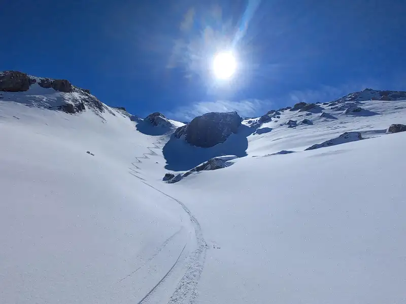 Verschneite Berglandschaft mit Spuren im Schnee und Sonnenschein.