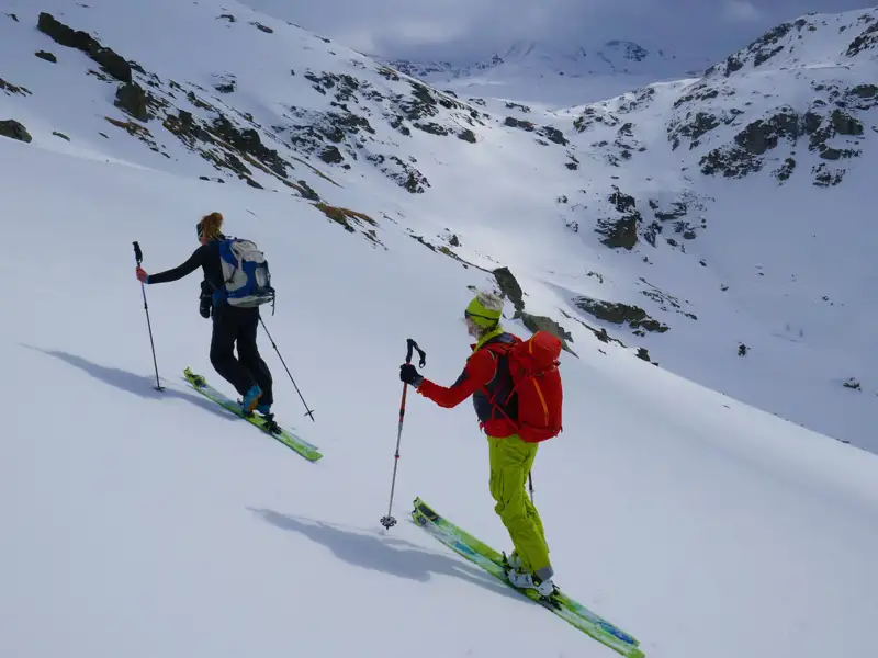 Zwei Skitourengeher fahren einen verschneiten Berg hinab.