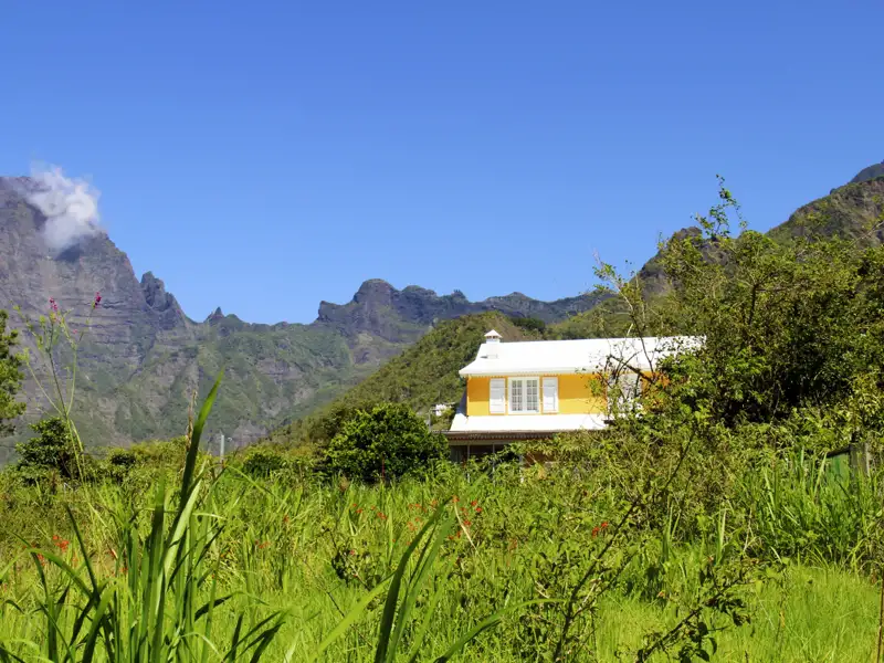Gelbes Haus mit weißer Dach in einer bergigen Landschaft.