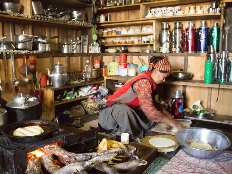 Zubereitung von Teigfladen in einer Küche mit traditionellen Kochutensilien und einem Holzfeuer.