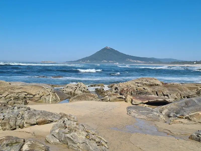 Felsiger Küstenabschnitt mit Blick auf einen Berg am Meer.