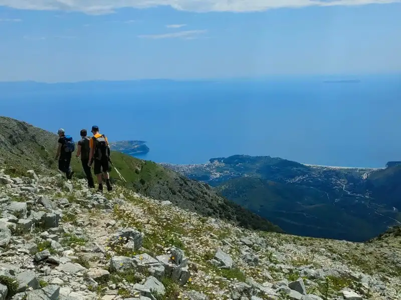 Wanderer auf einem Bergpfad mit Blick auf das Meer und eine Küstenstadt.