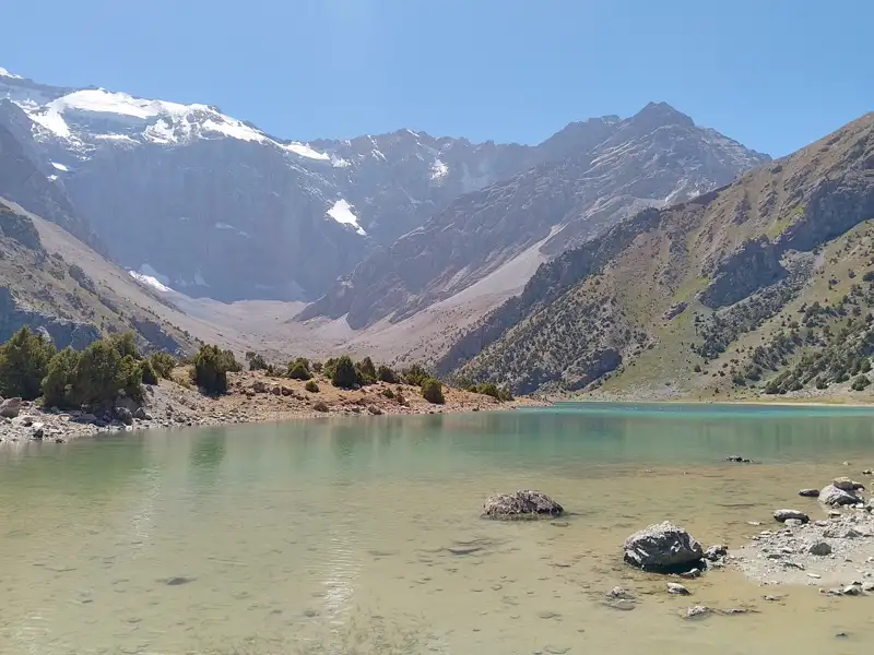 Panoramablick auf einen Bergsee mit schneebedeckten Gipfeln im Hintergrund.