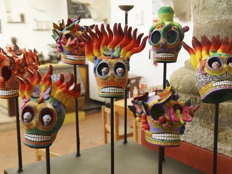 Bunte, verzierte Totenköpfe, ausgestellt auf einem Ständer. Die Schädel sind mit Flammen, Schmetterlingen und anderen Details verziert.