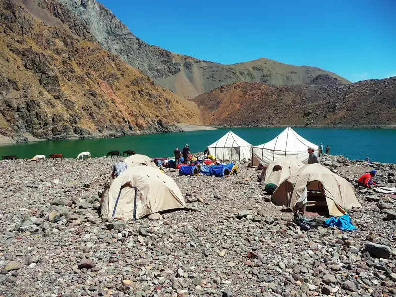 Zelte und Maultiere am Ufer eines Bergsees.