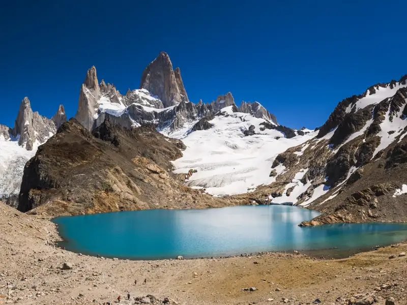 Panoramablick auf einen türkisblauen See, umgeben von schneebedeckten Bergen und Gletschern.