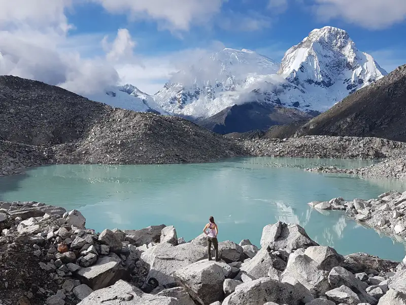 Türkisfarbener Bergsee mit schneebedeckten Gipfeln im Hintergrund.