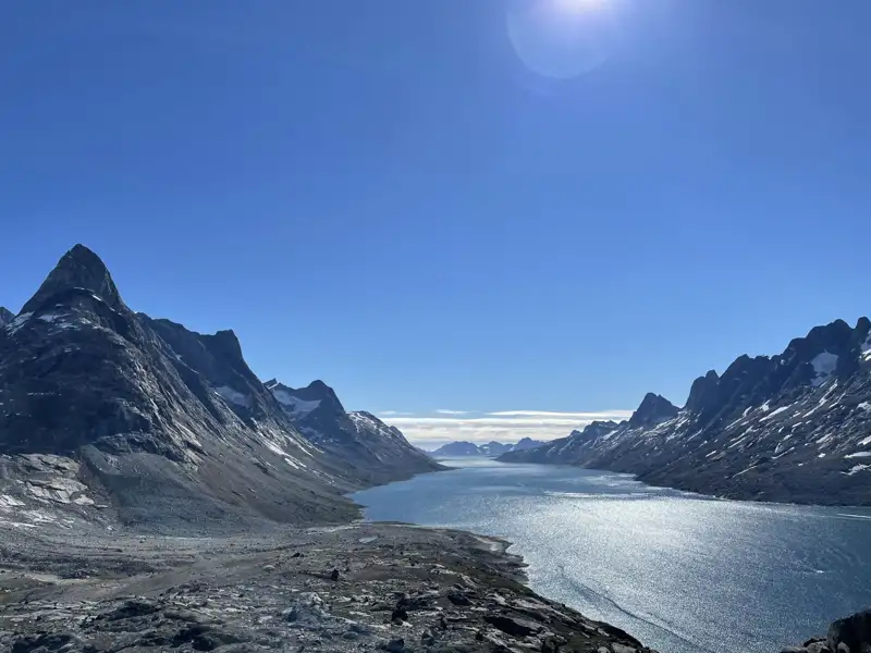 Panoramablick auf einen Fjord in Grönland mit Bergen und blauem Himmel.