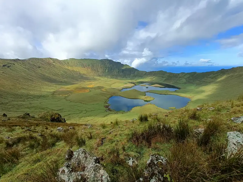 Vulkanischer Kratersee mit grüner Vegetation und umgebendem Kraterrand.