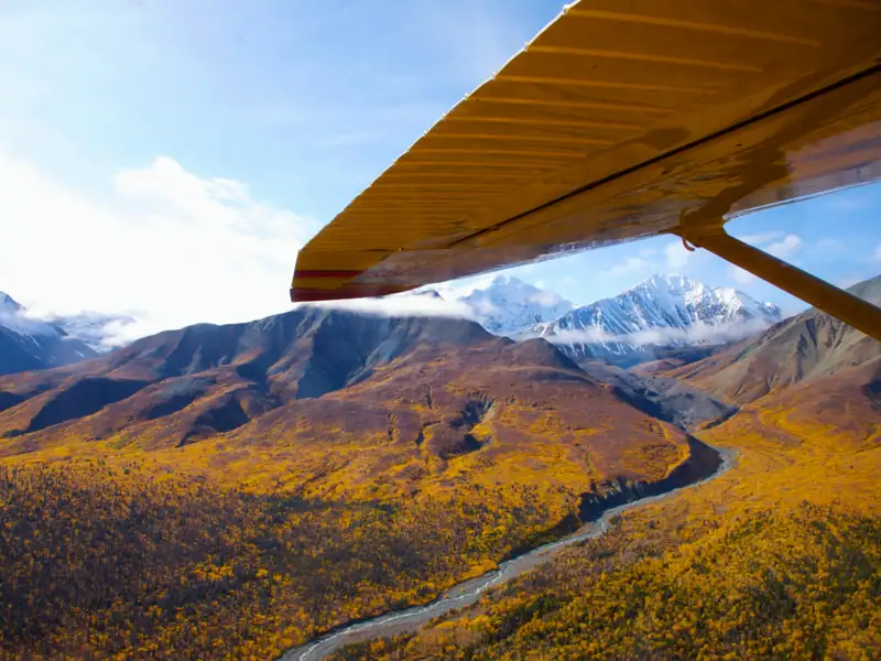 Flugzeugflügel und herbstliche Berglandschaft mit Fluss aus der Luftperspektive.