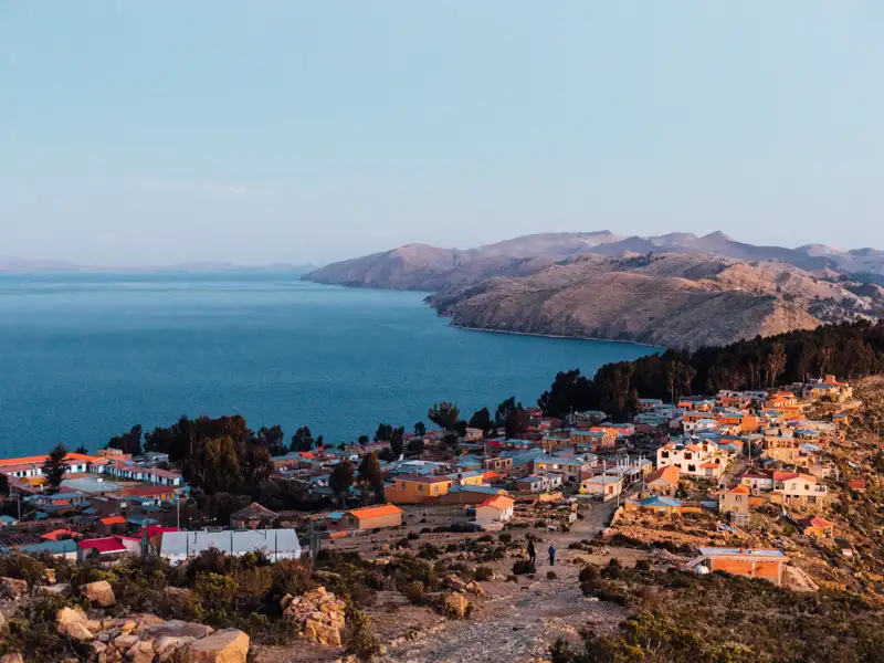 Blick auf eine Ortschaft am Titicacasee, umgeben von Hügeln.