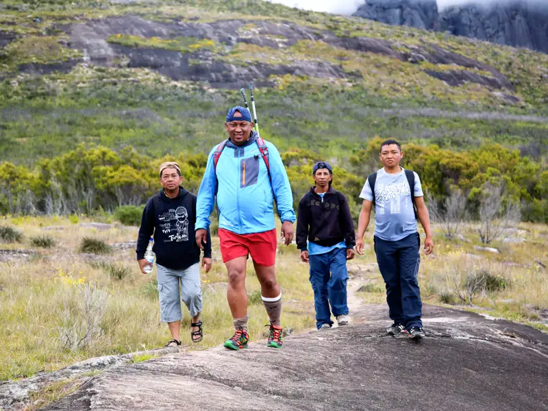 Vier Wanderer auf einem felsigen Wanderweg in den Hügeln.