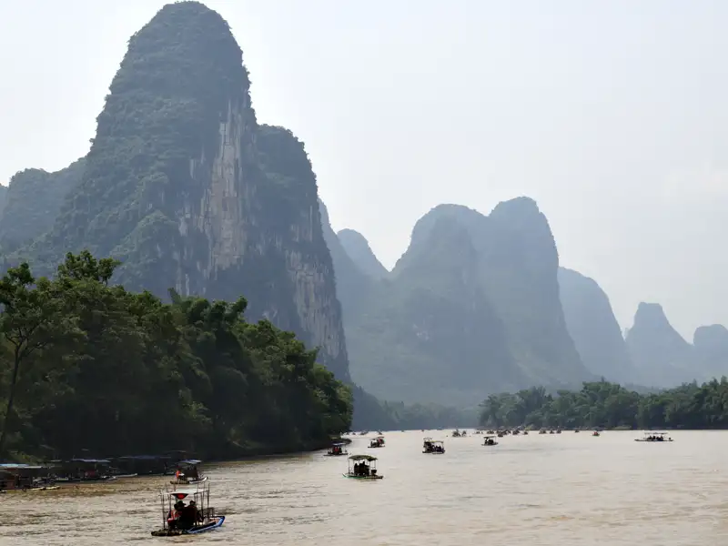 Traditionelle Boote fahren auf einem Fluss, umgeben von den charakteristischen Karstbergen.