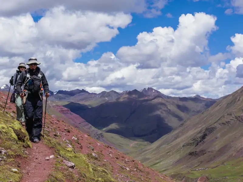 Zwei Wanderer auf einem Bergpfad mit Blick auf die umliegende Berglandschaft.