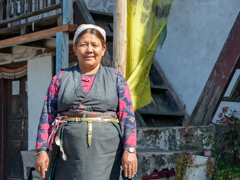 Einheimische Frau in traditioneller Kleidung vor einem Gebäude mit Gebetsfahne.