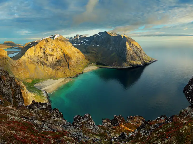 Panoramablick auf eine abgeschiedene Bucht mit türkisfarbenem Wasser und imposanten Bergen im Hintergrund.