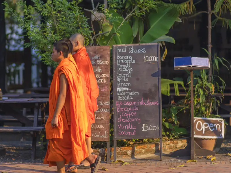 Zwei Mönche gehen an einer Speisekarte vorbei, die Fruchtshakes und Eiscreme-Shakes anbietet.