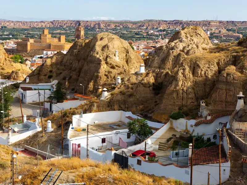 Traditionelle Höhlenwohnungen in Guadix, Spanien, mit der Stadt und der Burg im Hintergrund.