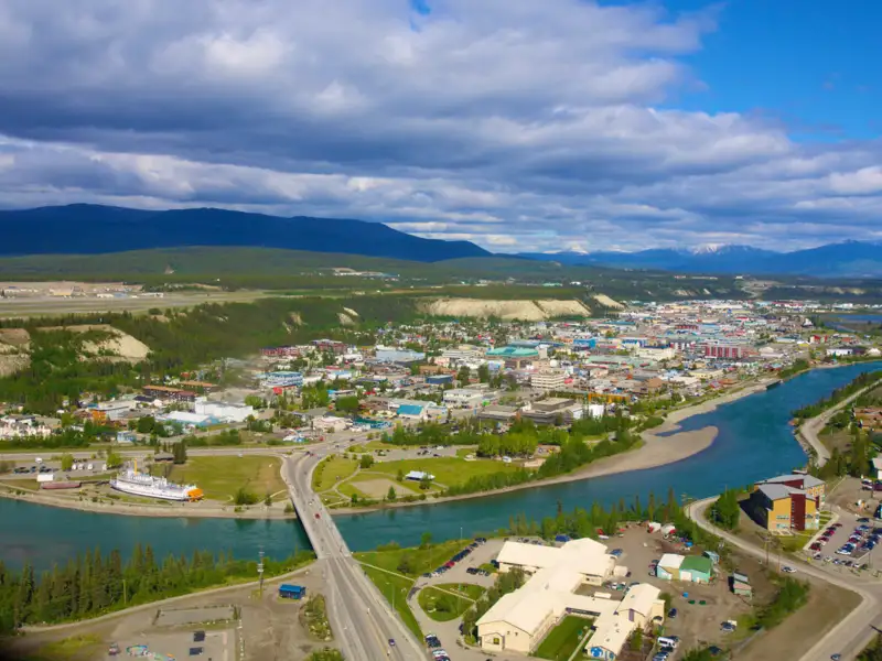 Panoramablick auf Whitehorse, Yukon, mit Fluss, Brücke, Gebäuden und Bergen.
